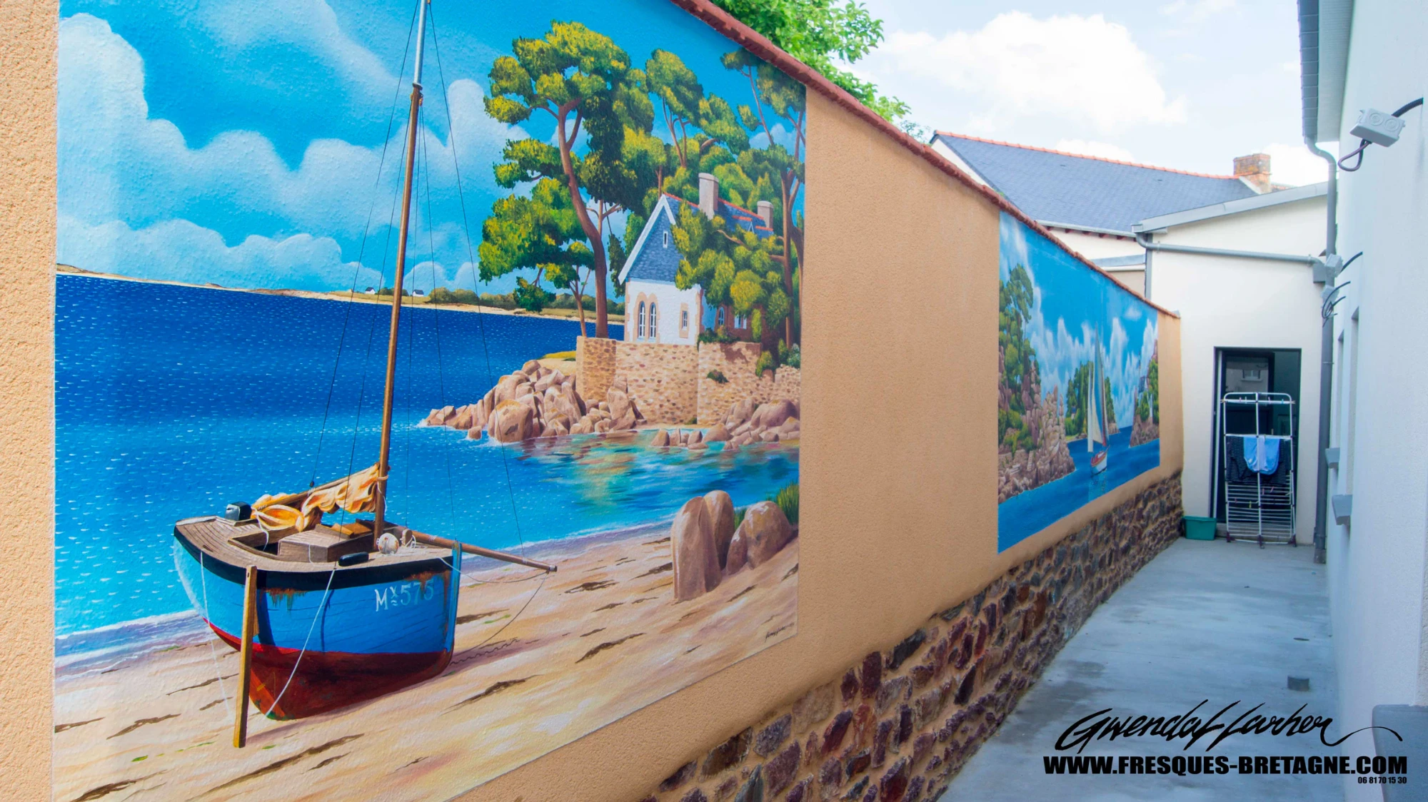Détail d'une plage, d'un bateau et d'une maison peints en trompe-l'œil sur un mur mitoyen de jardin à Bédée